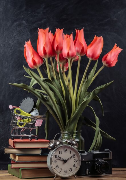 Bouquet de tulipes rouges et d'accessoires scolaires, appareil photo rétro sur fond de tableau noir à la craie. École nature morte