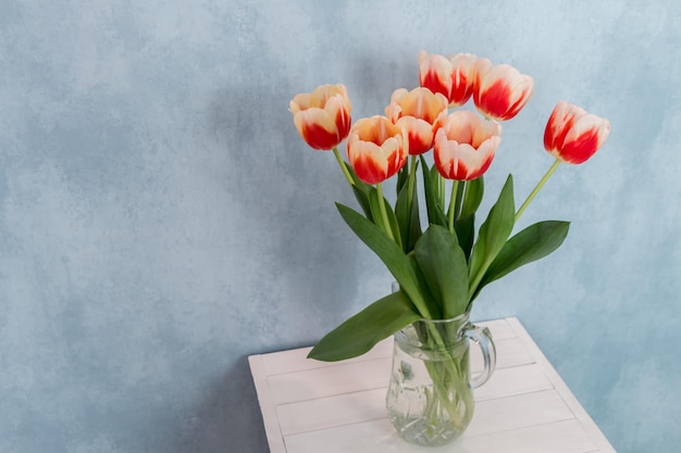 un bouquet de tulipes rouges et blanches dans un pichet en verre sur fond bleu sur un tableau blanc