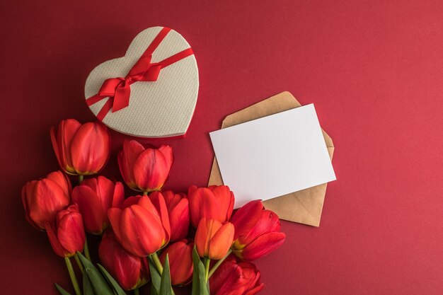 Bouquet de tulipes rouges et boîte de coeur cadeau isolé sur une surface rouge