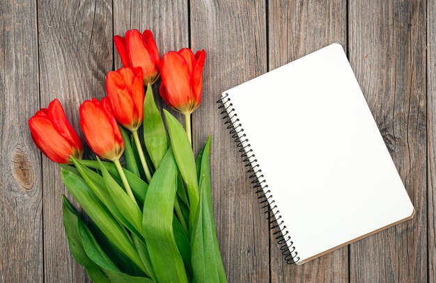 Bouquet de tulipes rouges et cahier sur une vue de dessus de fond en bois