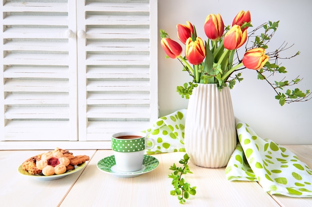 Bouquet de tulipes rouges, expresso dans une tasse verte à pois blancs et biscuits sur bois clair