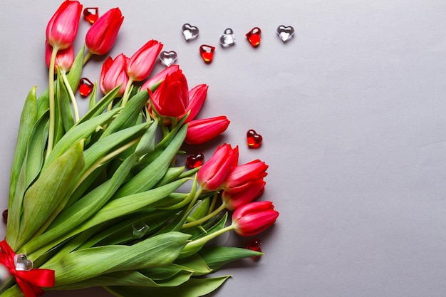 Le bouquet des tulipes rouges fraîches se trouve sur le fond gris diagonalement avec des coeurs en verre