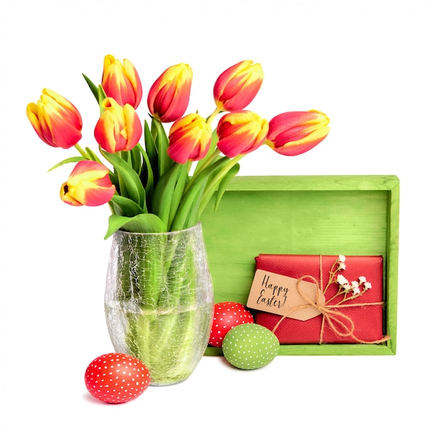 Bouquet de tulipes rouges, planche de bois, cadeau avec étiquette et oeufs de Pâques colorés sur blanc