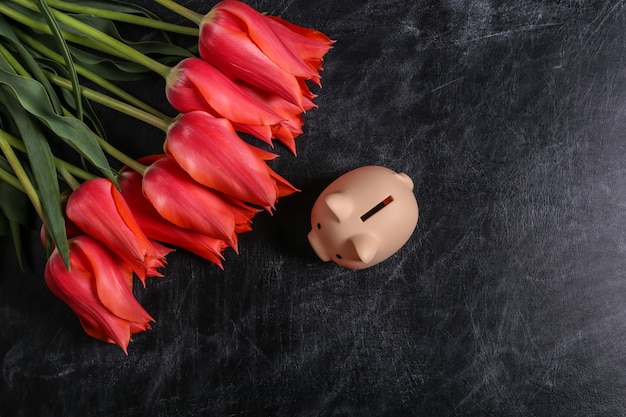 Bouquet de tulipes rouges et tirelire sur un fond de tableau