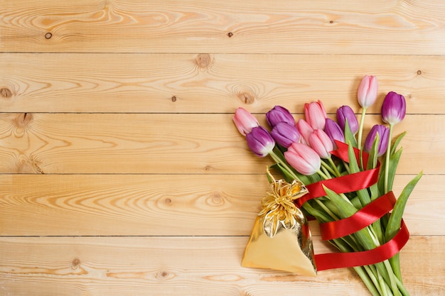 Bouquet de tulipes avec ruban rouge et cadeau dans un sac doré sur une texture en bois naturel