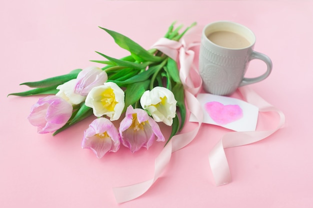 Bouquet de tulipes et une tasse de café sur un fond rose pastel.