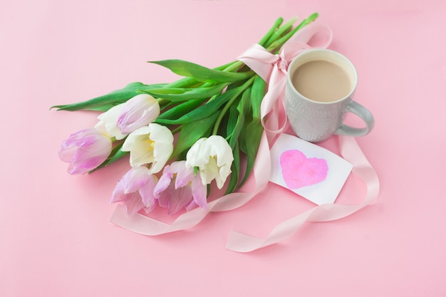 Bouquet de tulipes et une tasse de café sur un fond rose pastel.