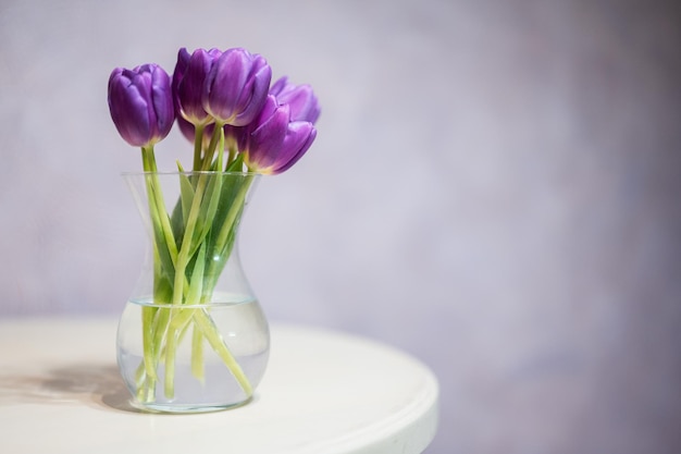 Bouquet de tulipes violettes avec des feuilles vertes dans un vase en verre