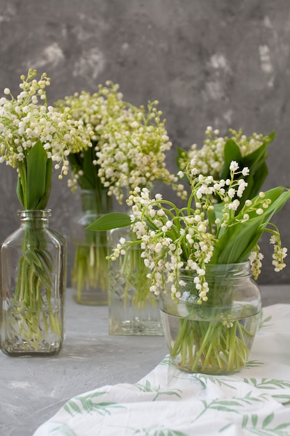 bouquets frais de muguets dans des vases en verre sur la nappe blanche sur fond gris