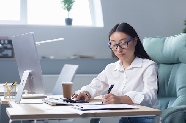 Bourreau de travail une belle jeune femme d'affaires asiatique à lunettes est très tôt au travail assis à la