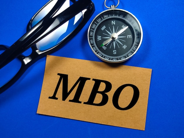 Boussole et lunettes avec word MBO Management By Objectives sur fond bleu Concept d'entreprise