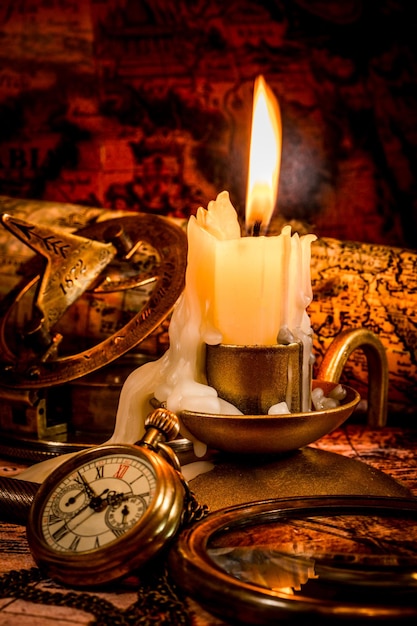 Boussole vintage, loupe, montre de poche, stylo plume, spyglass se trouvent sur une vieille carte ancienne avec une bougie allumée. Nature morte d'époque.