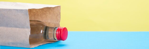 Bouteille d'alcool avec du liège rouge dans un sac en papier sur fond jaune et bleu.