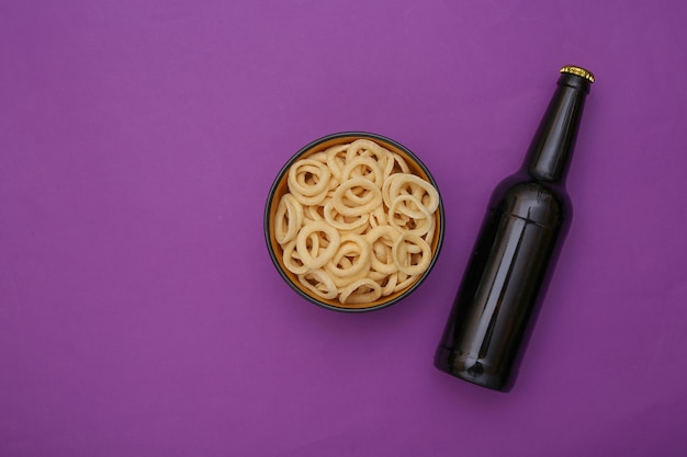 Bouteille de bière et un bol avec des anneaux de maïs sur fond violet. Vue de dessus