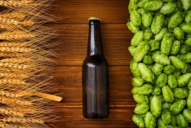 Photo une bouteille de bière sur un fond en bois avec du houblon vert et des épis de blé