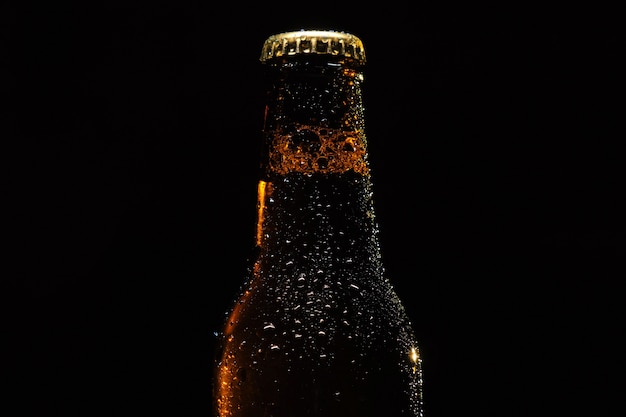 Bouteille de bière avec des gouttes d'eau gros plan sur un fond noir isolé.