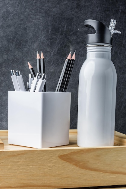Bouteille blanche en acier inoxydable avec crayon et stylos sur une boîte en bois