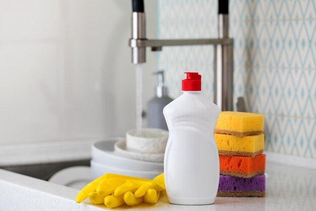 Photo une bouteille blanche avec des éponges de gel de lavage de vaisselle et des gants en caoutchouc