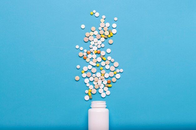 Bouteille blanche et pilules multicolores sur fond bleu. Concept de produits pharmaceutiques, de médicaments, de médicaments et de traitement des maladies. Mise à plat, vue de dessus