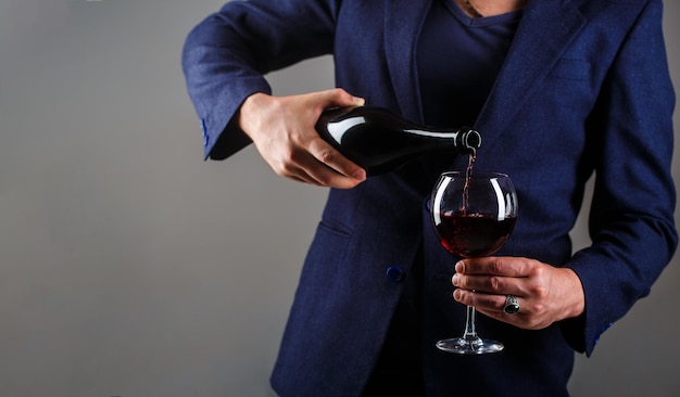 Bouteille de boisson gourmande, verre à vin rouge, sommelier, dégustation. Serveur versant du vin rouge dans un verre. Homme sommelier, dégustation, cave, vigneron masculin. Le vin rouge est versé de la bouteille au verre.