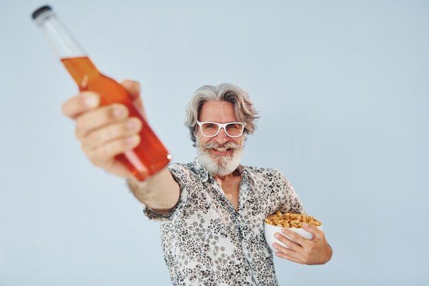 Bouteille de boisson et pop-corn dans les mains Senior homme moderne et élégant aux cheveux gris et à la barbe à l'intérieur