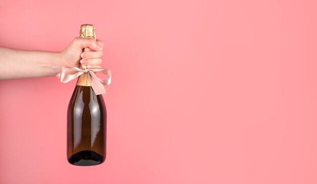 Une bouteille de champagne avec un arc sur fond rose