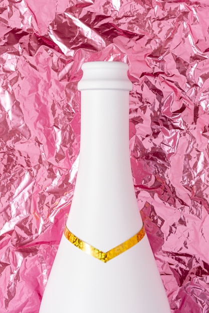 Bouteille de champagne blanc sur une surface en aluminium froissé rose.