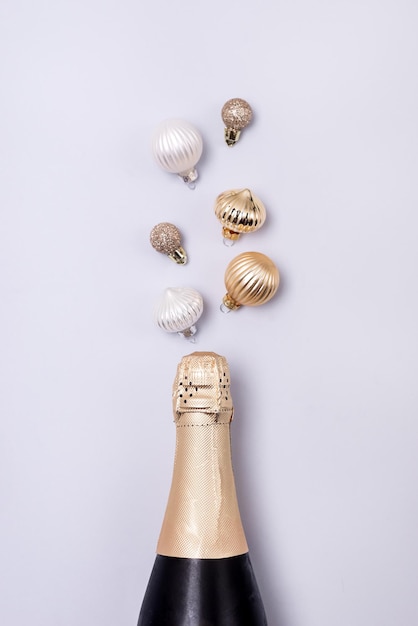 Bouteille de champagne avec des boules de Noël blanches et dorées Fond bleu Mise à plat Vue de dessus Concept de vacances à la mode verticale