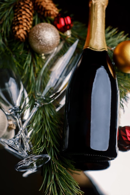 Photo bouteille de champagne dans les branches d'un arbre de noël avec des verres et des cônes avec un arrière-plan flou