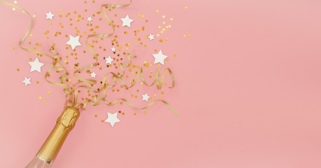 Bouteille de champagne avec des étoiles de confettis et des banderoles de fête dorées sur fond abstrait rose. Concept de nouvel an, Noël, anniversaire ou mariage. Copyspace vue de dessus horizontale Mise à plat.