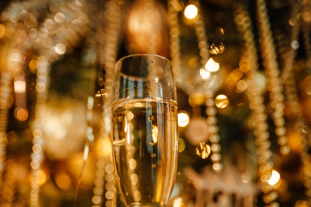 Photo bouteille de champagne avec des paillettes dorées et des verres avec des guirlandes jaune bokeh étincelantes