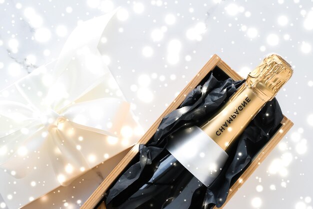 Photo bouteille de champagne de vacances de noël et une boîte-cadeau et neige brillante sur fond de marbre