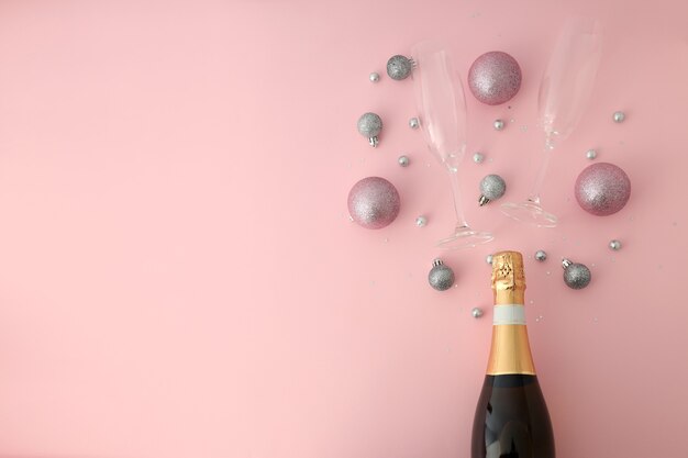 Bouteille de champagne, verres et boules sur fond rose.