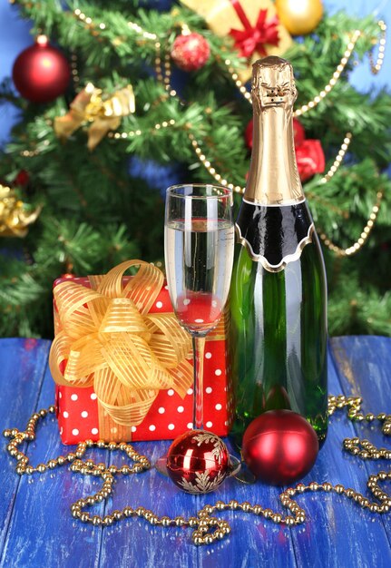 Bouteille de champagne avec verres et boules de Noël sur table en bois sur fond d'arbre de Noël