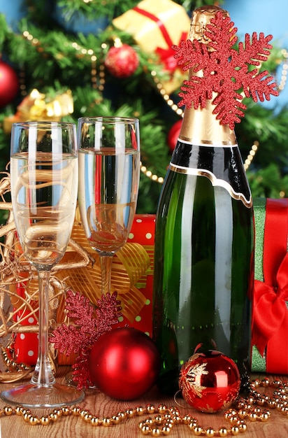 Bouteille de champagne avec verres et boules de Noël sur table en bois sur fond d'arbre de Noël