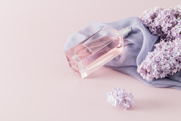 Une bouteille chic de parfum féminin ou d'eau de parfum se trouve sur l'accessoire d'une femme une écharpe et des fleurs lilas espace pour texte fond rose