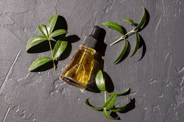 Une bouteille cosmétique en verre avec un sérum ou une huile pour le visage sur un fond sombre avec des herbes vertes. Concept de produits cosmétiques respectueux de l'environnement. Espace de copie.