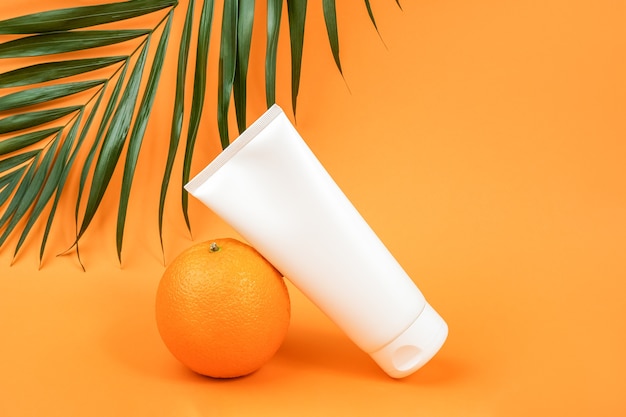 Bouteille cosmétique vierge blanche, tube de crème, lotion pour le corps, le visage ou la main, fruit orange et branche de palmier. Concept cosmétique avec vitamine C, antioxydants ou anti-cellulite. Vue de face de la maquette.