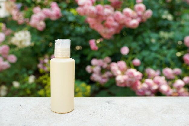 Bouteille de cosmétiques jaune sur du béton près de fleurs roses