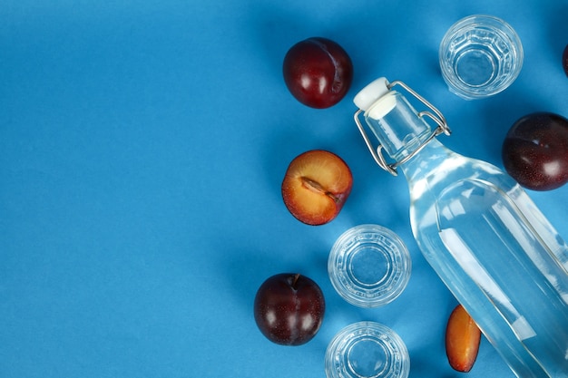 Bouteille et coups de vodka aux prunes et ingrédients sur fond bleu