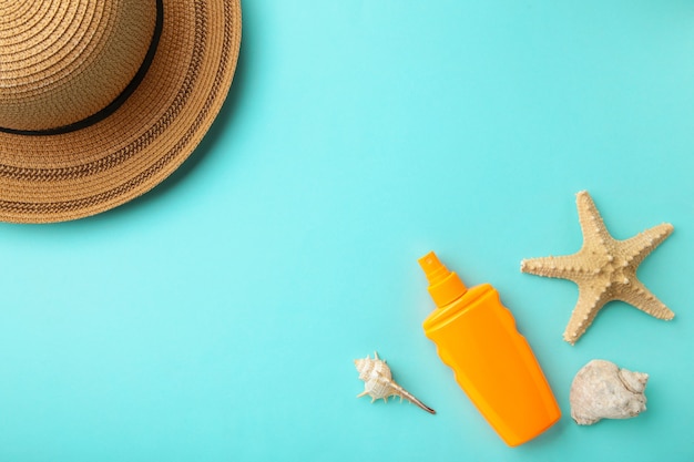 Bouteille de crème solaire avec chapeau et coquilles sur fond bleu