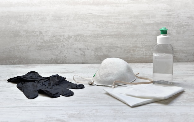 Bouteille de désinfectant pour les mains sur des mouchoirs à côté d'un masque anti-poussière sur une table en bois blanc