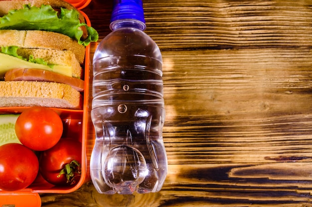 Bouteille d'eau et boîte à lunch avec sandwichs concombres et tomates sur table en bois Vue de dessus