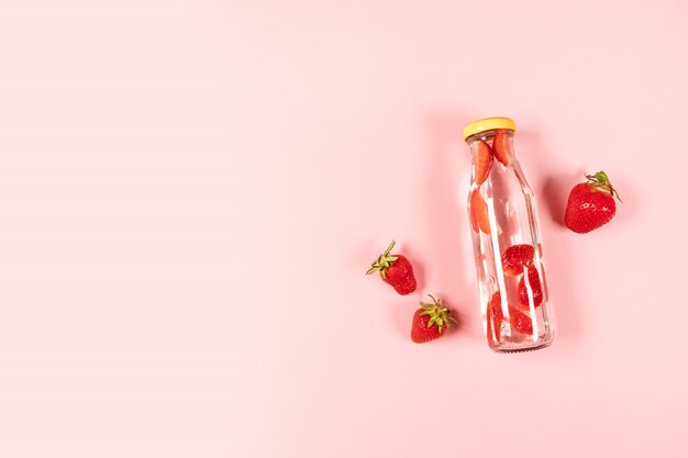 Bouteille d'eau détox, cocktail, limonade ou thé avec des fruits d'été aux fraises fraîches sur fond rose. Composition d'été, style minimal