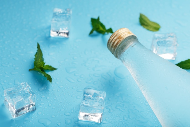 Bouteille d'eau froide, glaçons, gouttes et feuilles de menthe