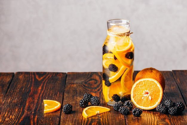 Bouteille d'eau infusée d'orange crue tranchée et de mûre fraîche. Ingrédients sur table en bois.