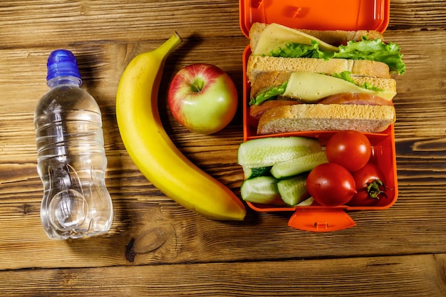 Bouteille d'eau pomme banane et boîte à lunch avec sandwichs et légumes frais sur une table en bois Vue de dessus