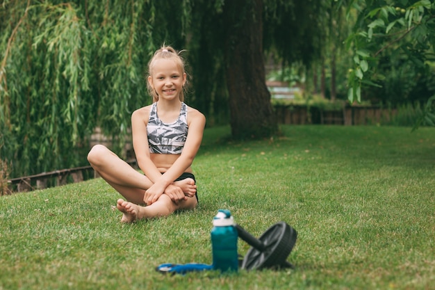 Une bouteille d'eau, une roue pour le sport, des cloches de bouilloire et la jeune fille au repos après avoir terminé un entraînement en ligne