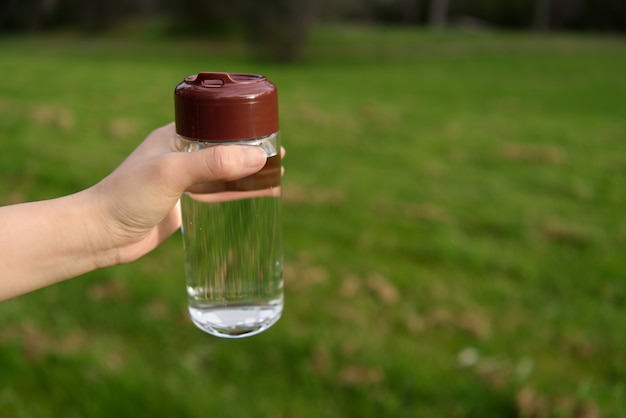 Une bouteille d&#39;eau tenue par une main féminine sur fond de nature.