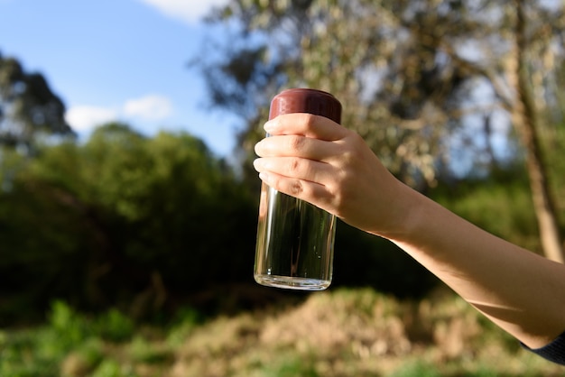 Une bouteille d&#39;eau tenue par une main féminine sur fond de nature.